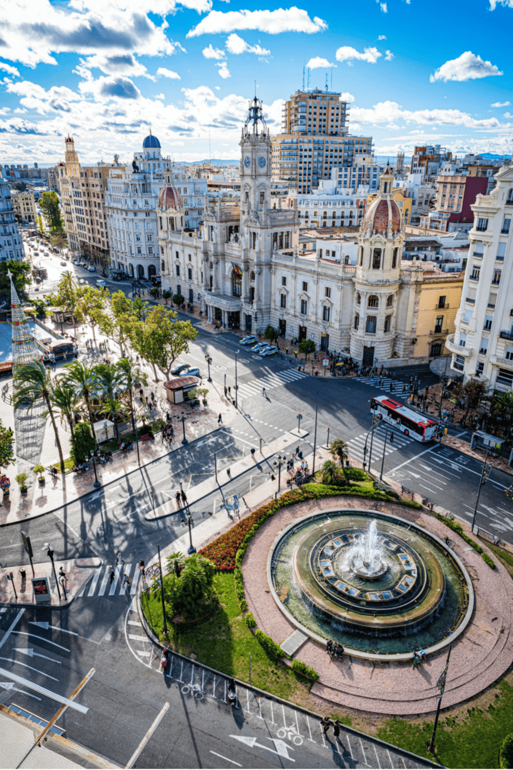 Historic city square with classic architecture, fountain, and bustling streets in daytime.