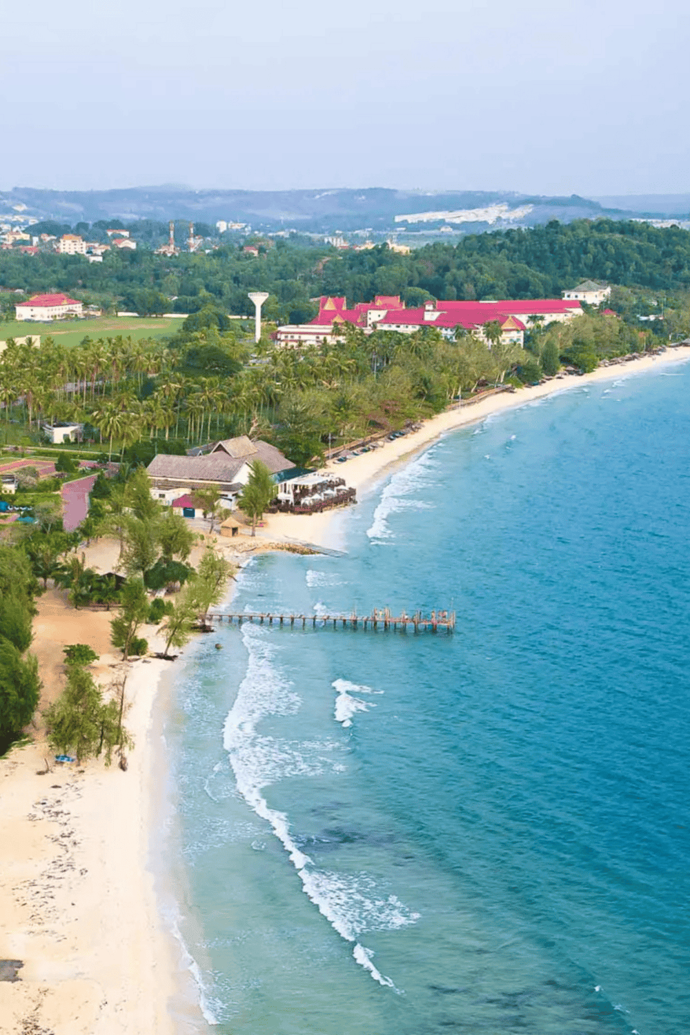 Serene coastal view of a tropical beach with lush greenery and resort buildings in the background.