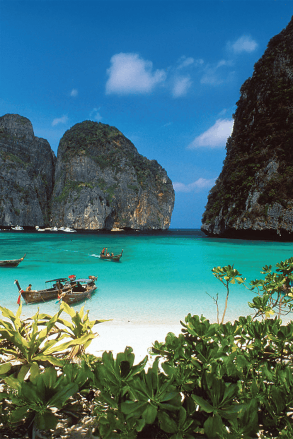Stunning tropical beach with turquoise waters, lush cliffs, and boats at a popular travel destination in Thailand.