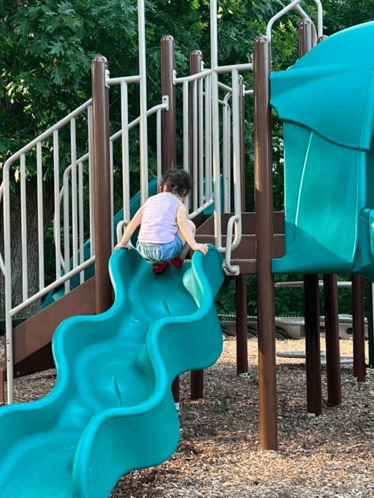 Child climbing playground slide at outdoor park for kids' recreation and fun.