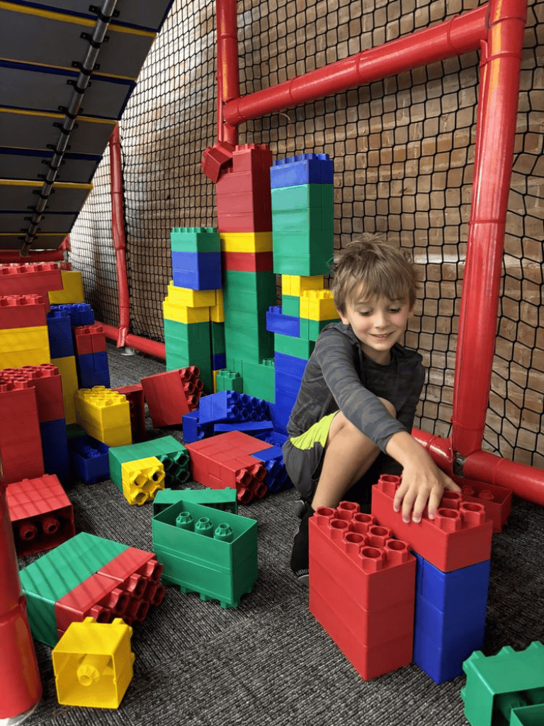Big kid building with large LEGO bricks at indoor play area.