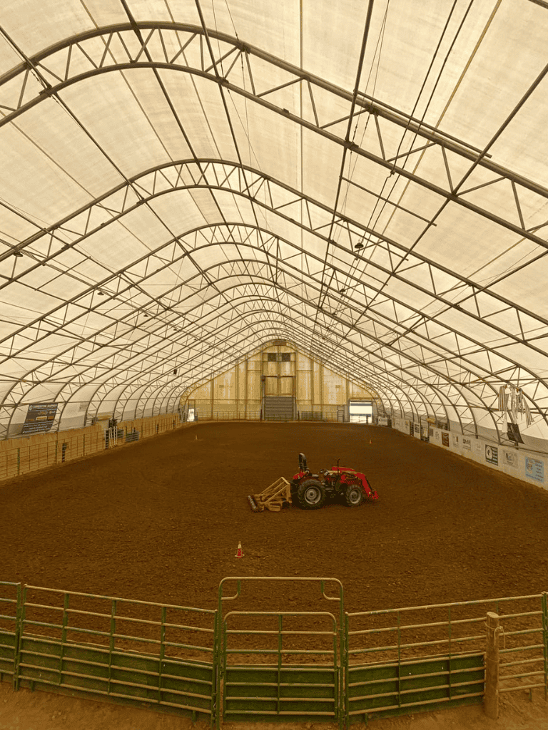 Covered arena with tractor leveling dirt surface for equestrian events or farm work.