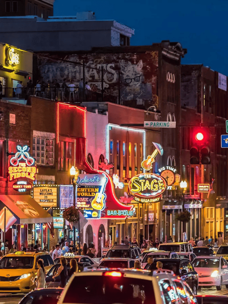 Vibrant street scene at night in Nashville with colorful neon signs and lively crowd, showcasing the bar and music district.