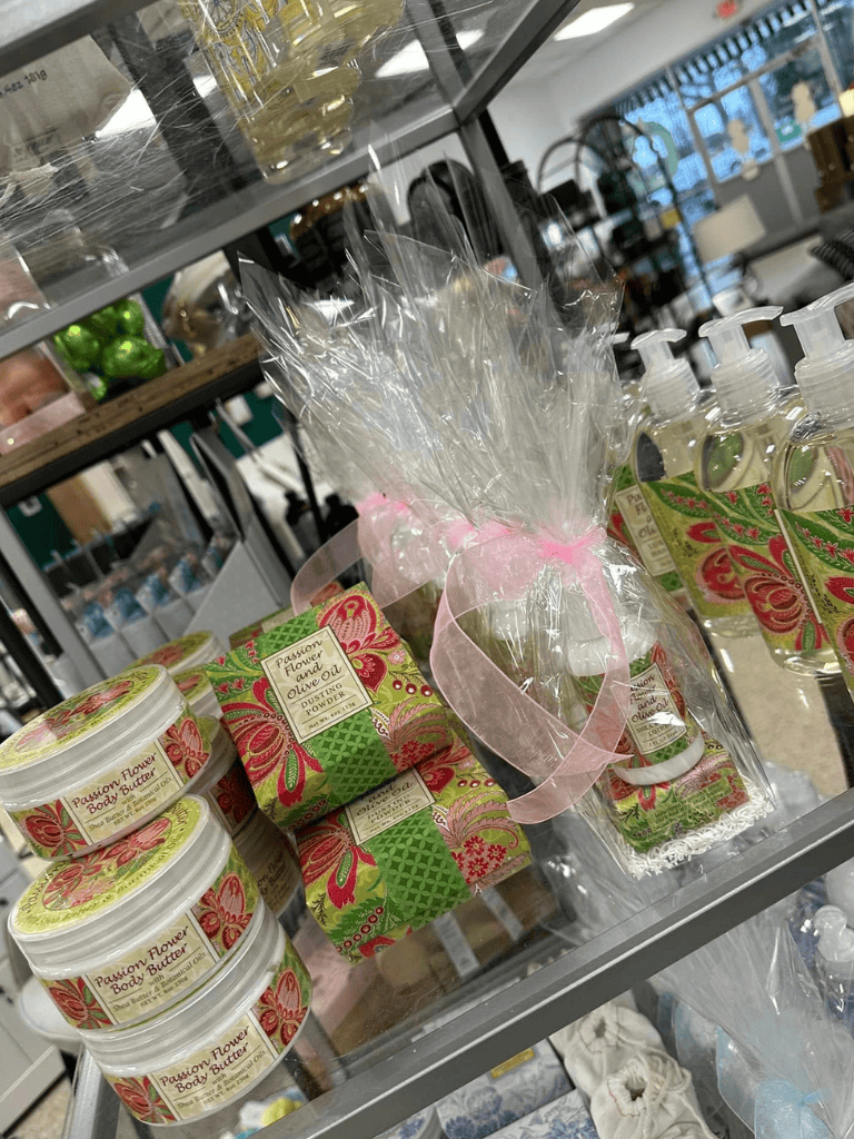White body butter jars with pink, green, and red floral packaging, gift-wrapped soap and hand sanitizer bottles in a store display.