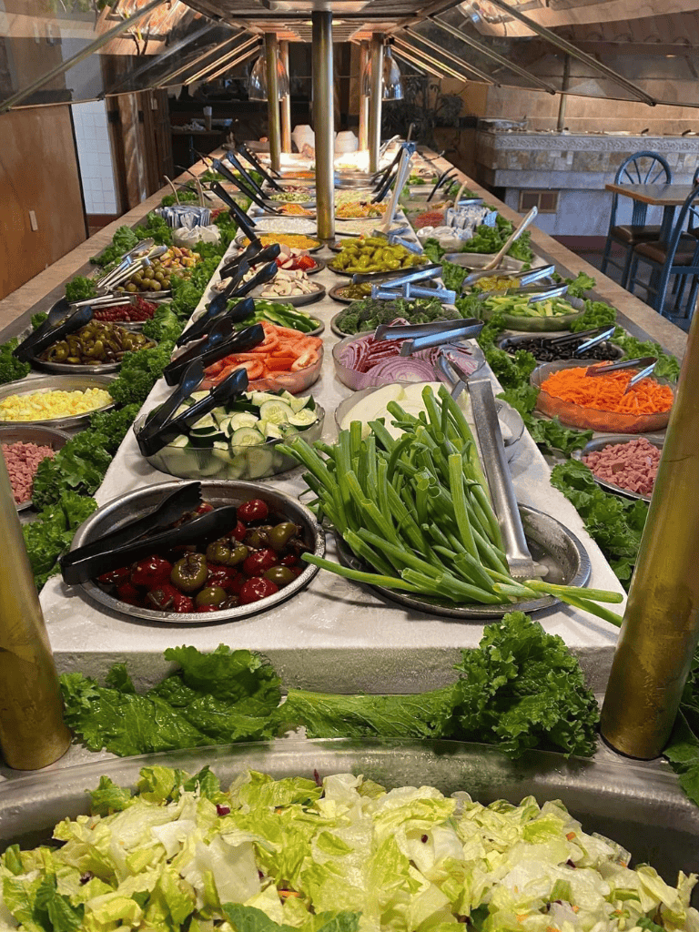 Fresh vegetable salad bar with leafy greens, peppers, tomatoes, onions, and olives at QuestForDirections.
