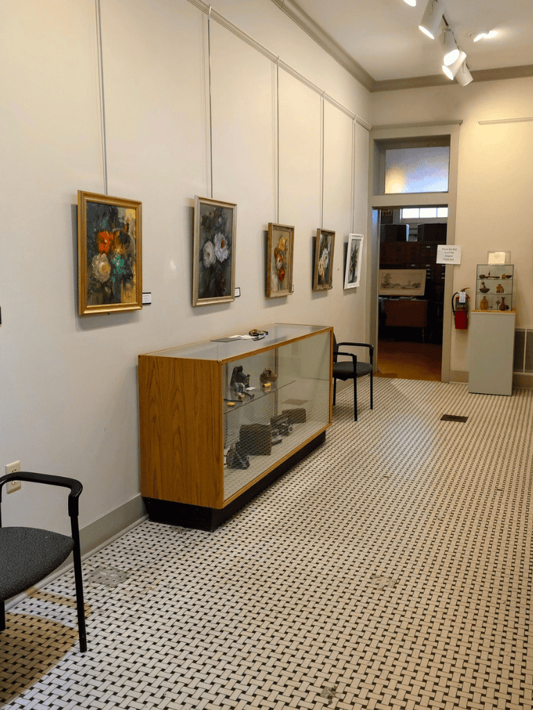 Colorful flower paintings displayed in an art gallery with a glass showcase and seating area.