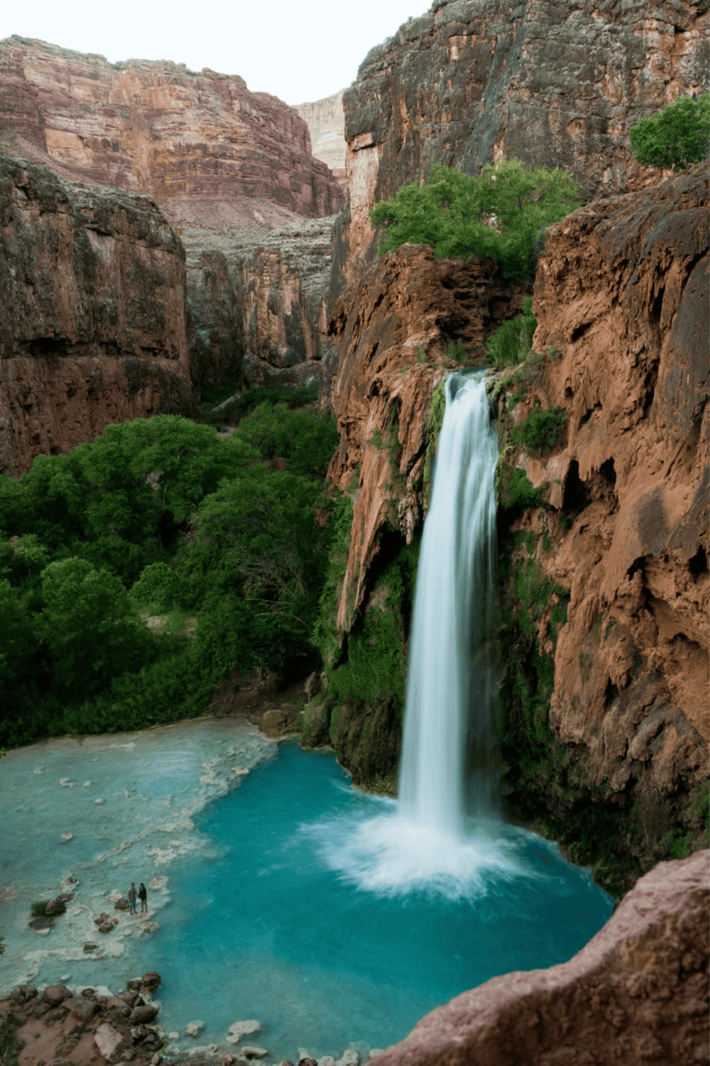 Serene waterfall in Grand Canyon, Arizona, surrounded by lush green trees and rugged canyon cliffs.