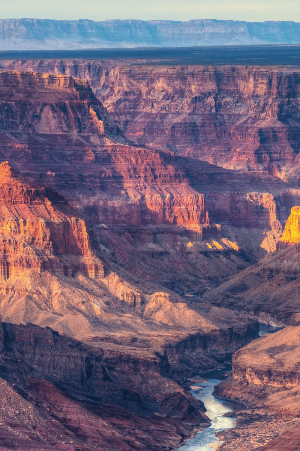 Colorful Grand Canyon at sunset, showcasing layered rock formations and the Colorado River.