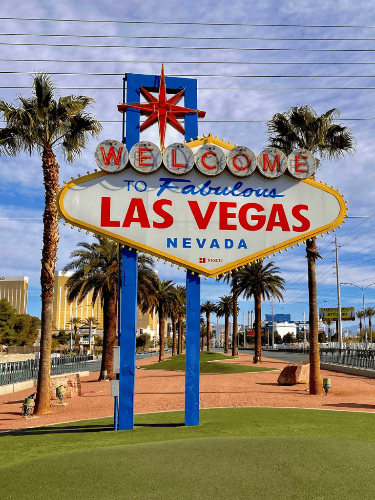 Welcoming Las Vegas sign with palm trees and cityscape in background.