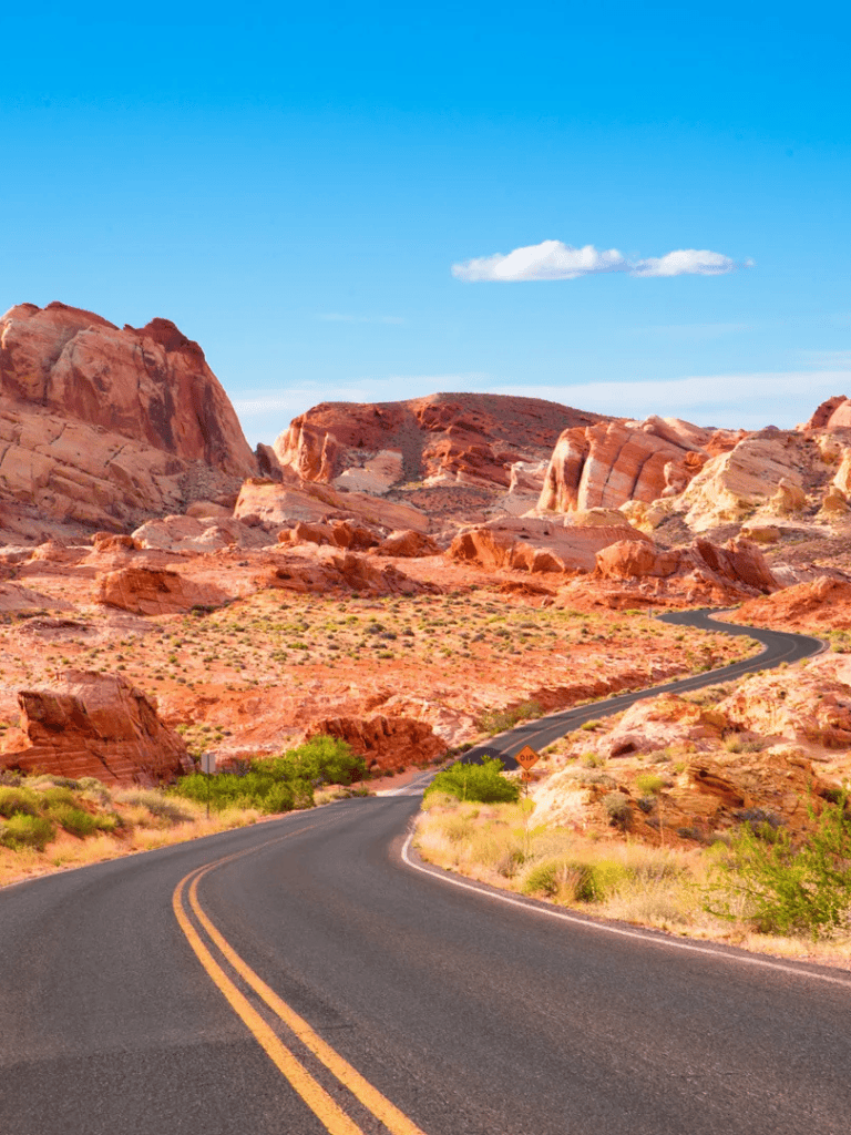 Vast desert landscape with winding road and red rock formations under blue sky.