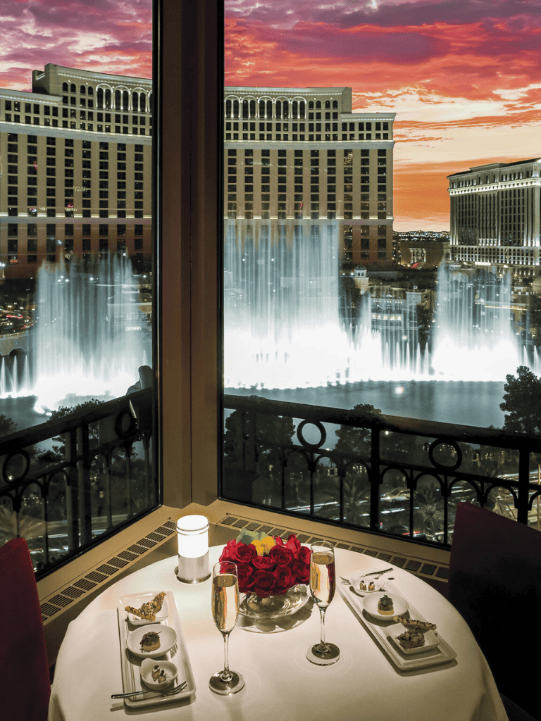 Elegant Las Vegas hotel window view of the Bellagio fountains at sunset for romantic dining experience.