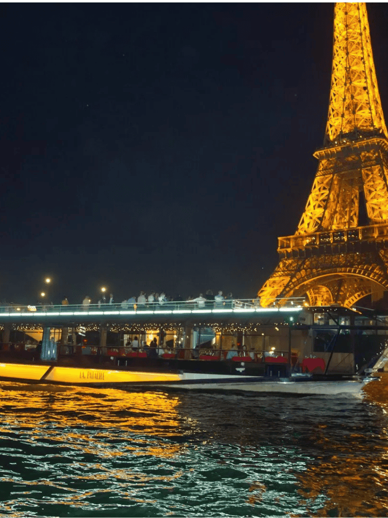 Night view of the Eiffel Tower illuminated in Paris, France, with a river cruise boat on the Seine at night.
