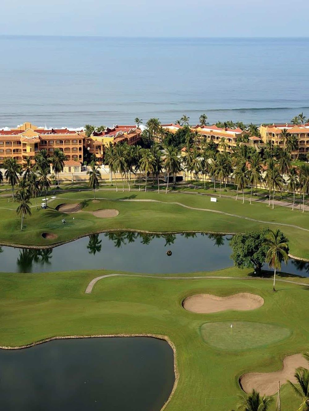 Stunning oceanfront golf course scene with tropical palm trees and resort buildings by the beach.