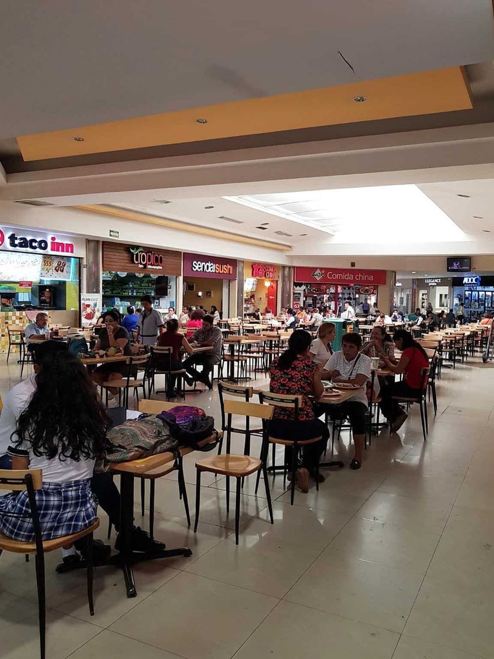 Bright food court inside a shopping mall with various Asian cuisine options and patrons dining.