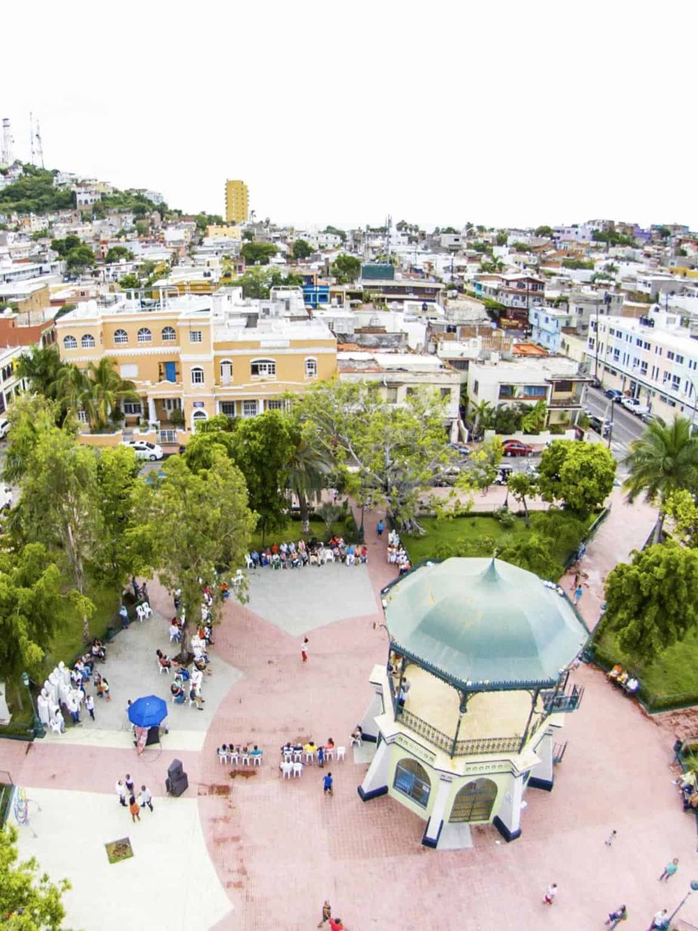 Colorful city square with park and gazebo in Mexico City, featuring vibrant urban buildings and green trees.
