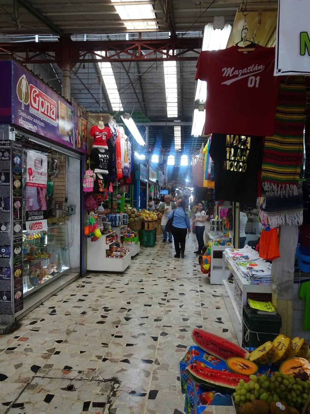 Colorful indoor market with stalls selling clothing, souvenirs, and fresh fruits, bustling shopping environment in Mexico.