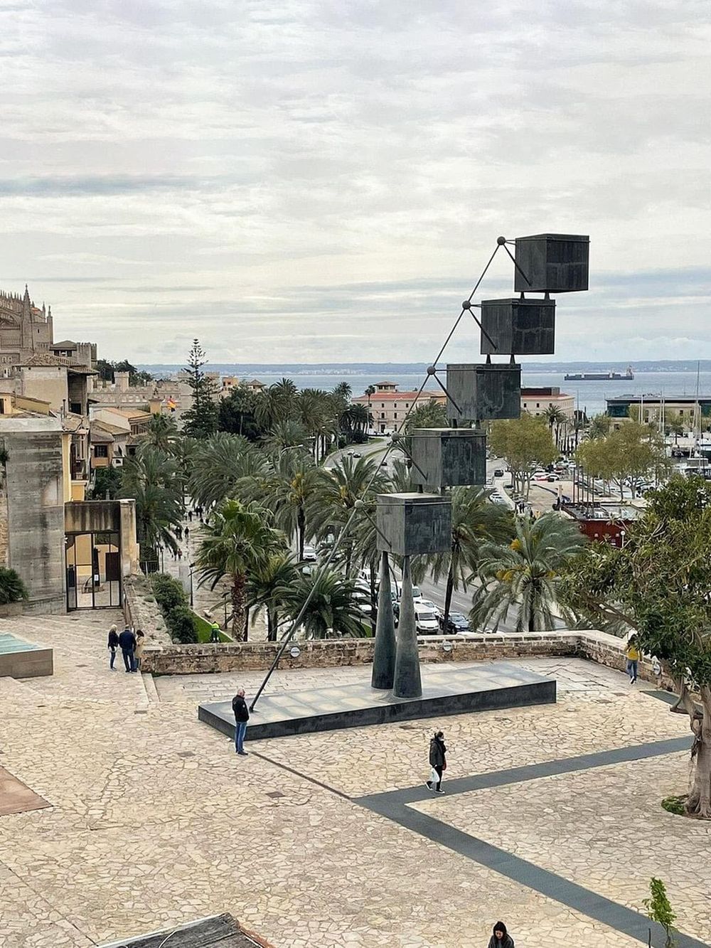 Modern outdoor sculpture with geometric black boxes along a scenic coastal cityscape.