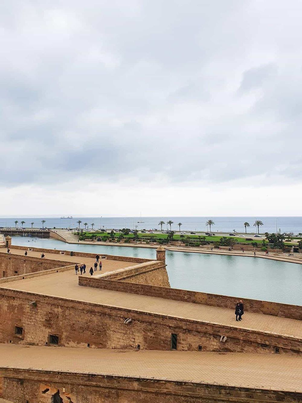 Panoramic view of historic fortress overlooking the ocean, with palm trees and cloudy sky, perfect for travel and exploration.