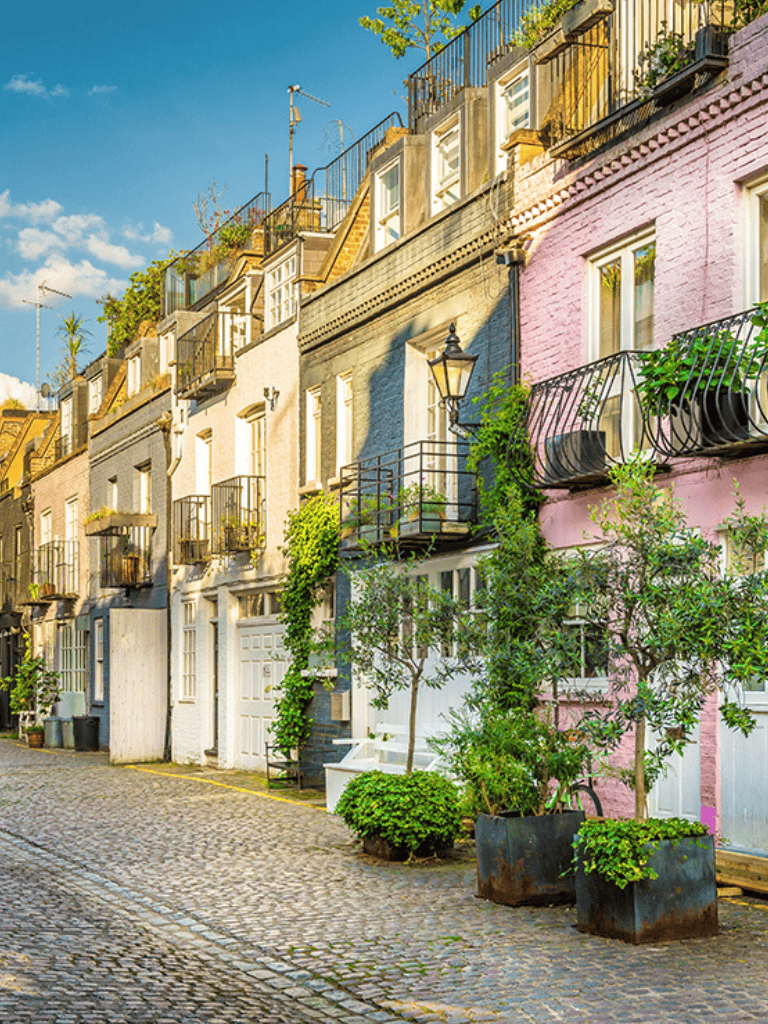 Colorful London row houses with balconies and greenery on cobblestone street under blue sky.