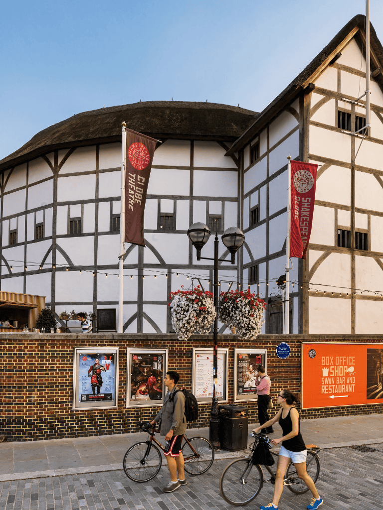 Colorful street scene at Shakespeare's Globe Theatre, London, with pedestrians and bikers in front of historic attraction.