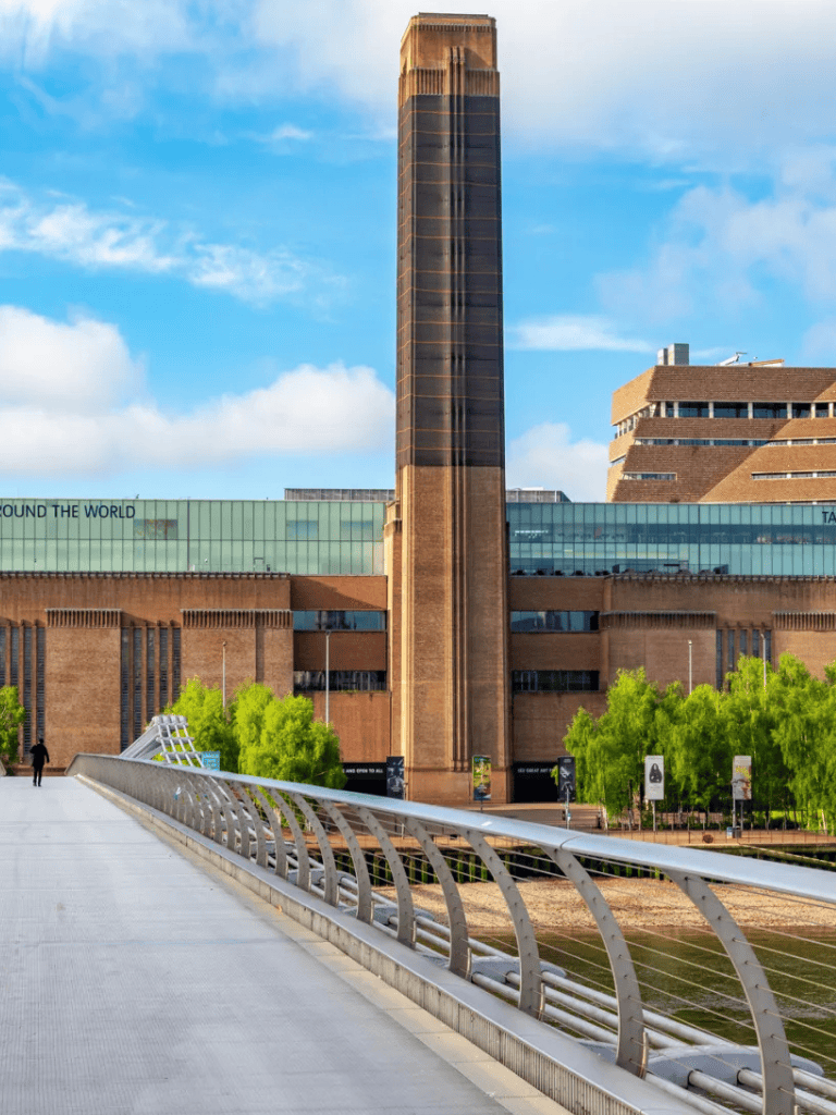 Modern city skyscraper with urban park and pedestrian bridge in the foreground.