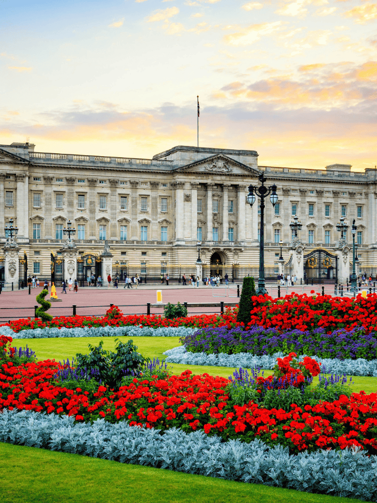 Aerial view of Buckingham Palace with vibrant flower gardens and sunset sky in London.