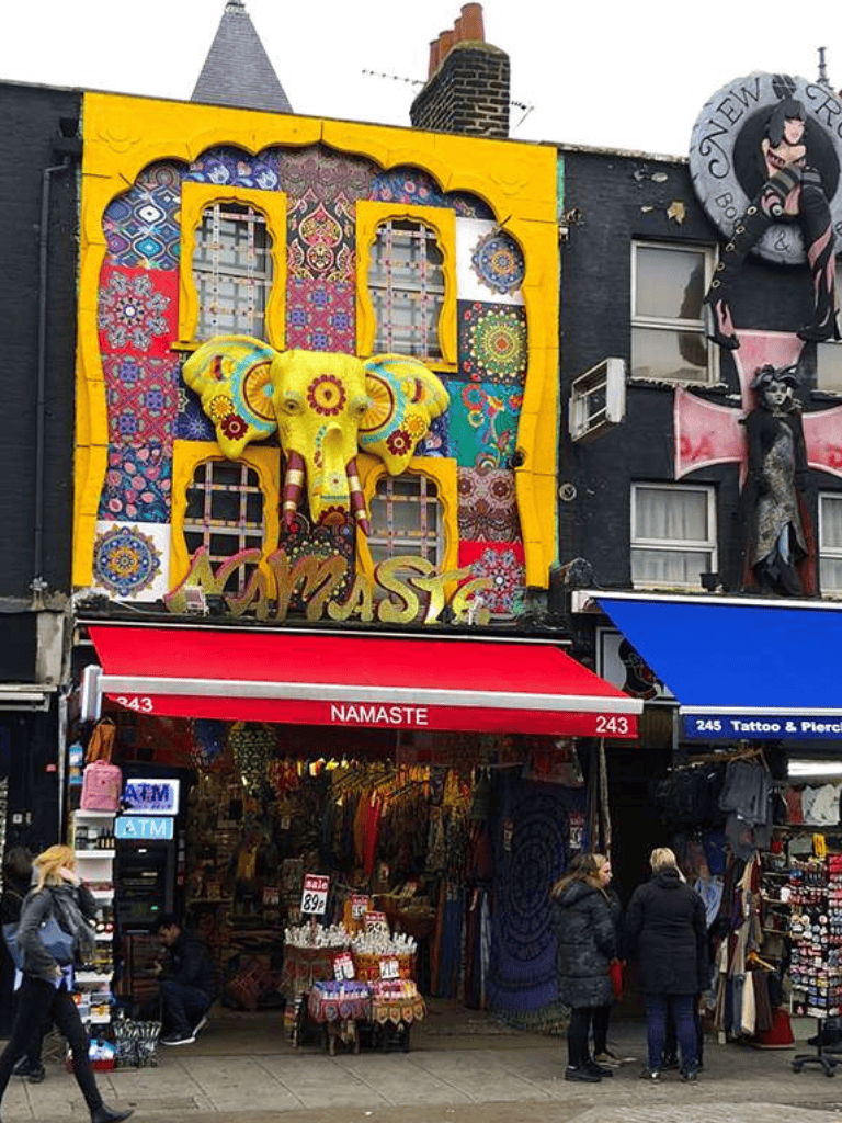 Vibrant storefront with colorful mural, elephant sculpture, and shopping boutique on a busy street.