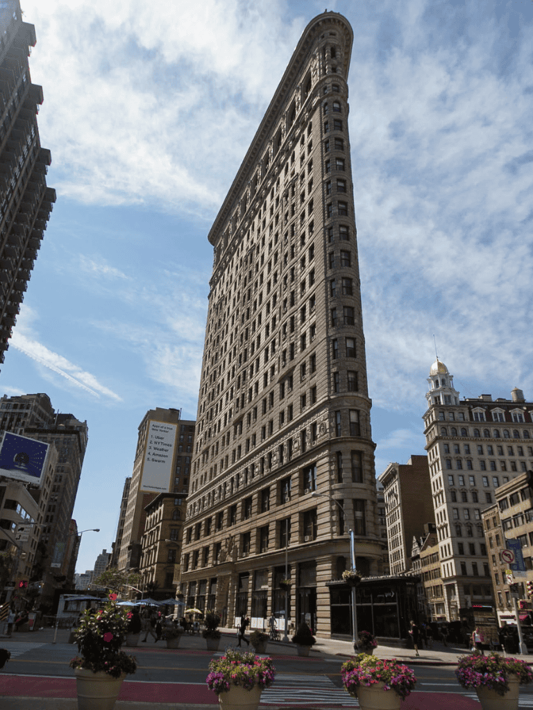 New York City Flatiron Building with blue sky and city street scene, ideal for travel and directions.