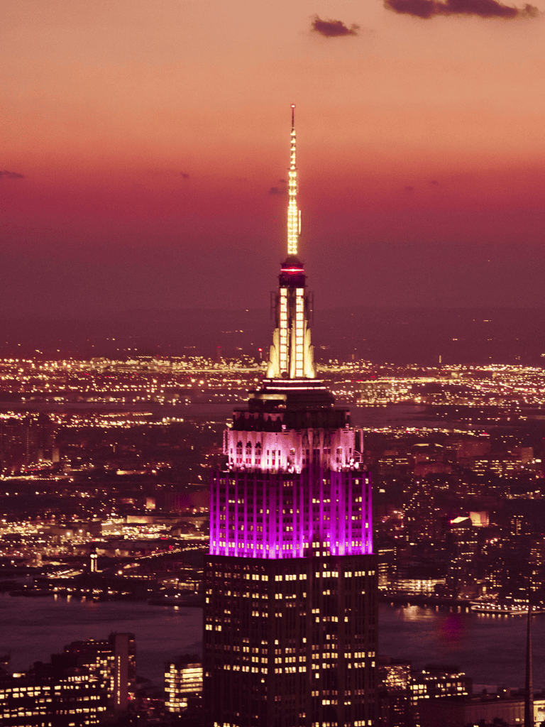 Brightly lit Empire State Building at sunset, showcasing an iconic NYC skyline and city lights, perfect for NYC travel guides.