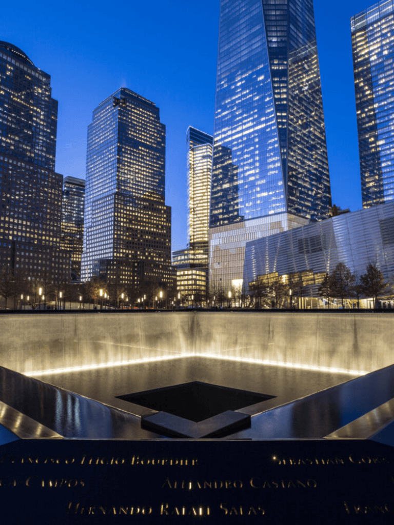 Empty memorial pool at 9/11 Memorial with city skyline at dusk, New York City.