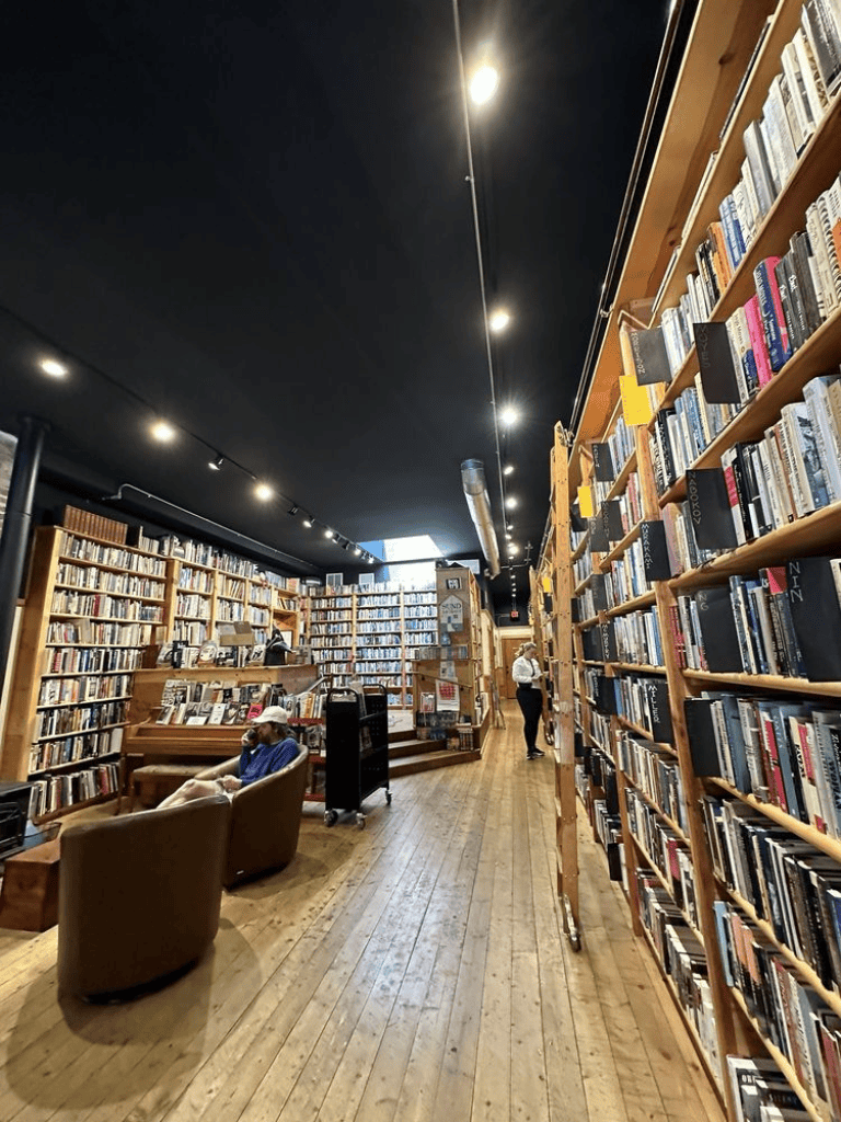 Cozy bookstore interior with wooden shelves, reading chairs, and customers browsing books.