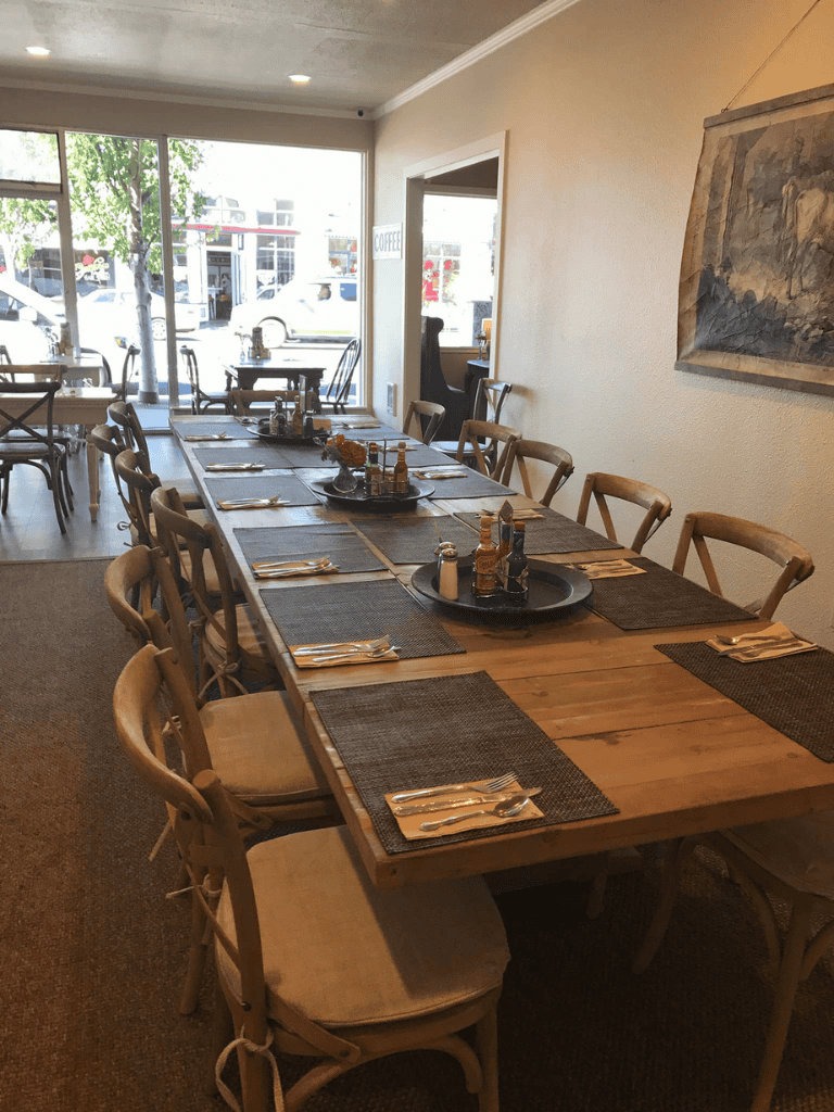 Cozy restaurant with wooden tables and chairs, large windows, and inviting dining atmosphere.