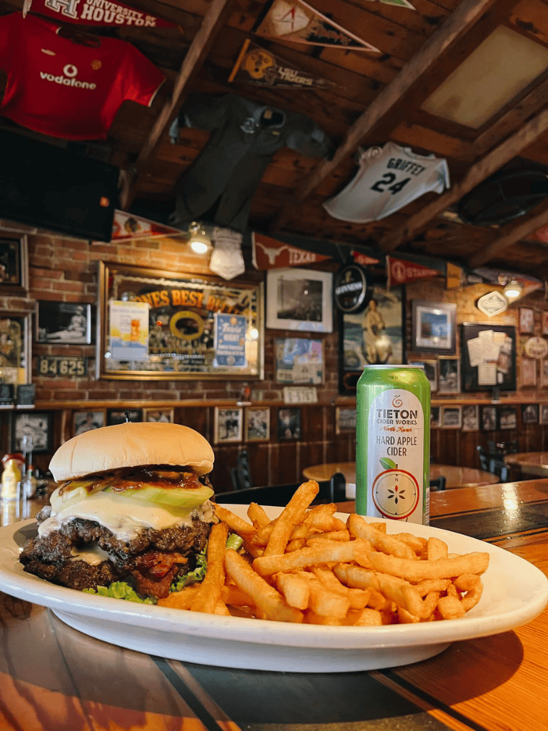 Juicy cheeseburger with fries and apple cider in a rustic sports bar setting, perfect for a casual meal.