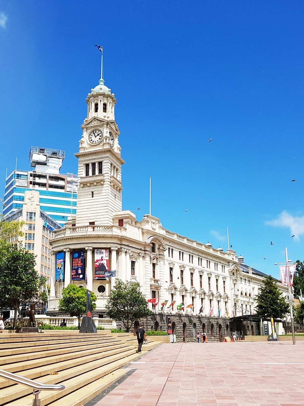 Historic clock tower building in downtown with clear blue sky and modern surroundings.
