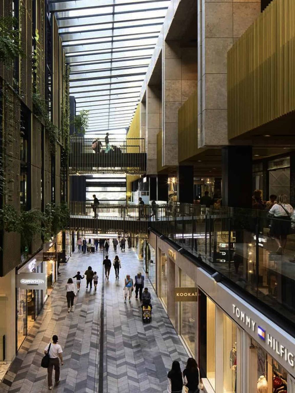 Bright shopping mall interior with high glass ceiling and luxury retail stores.