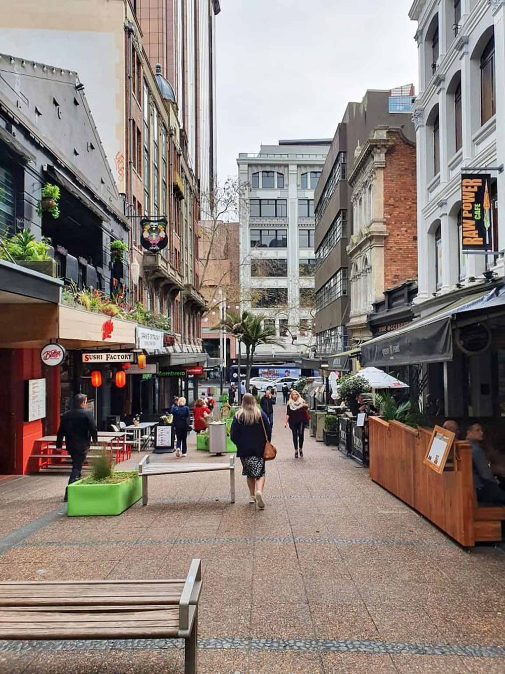 Vibrant city street with restaurants, shops, pedestrians, and modern buildings, urban dining and shopping scene.