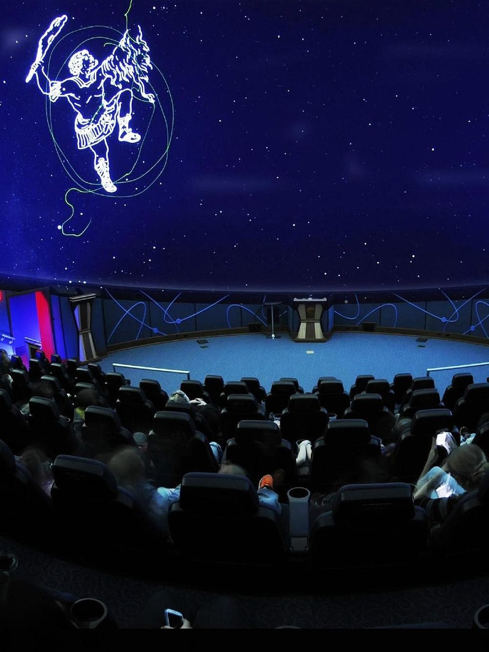 Ancient Greek constellation diagram in a planetarium showing Orion across a starry sky background.