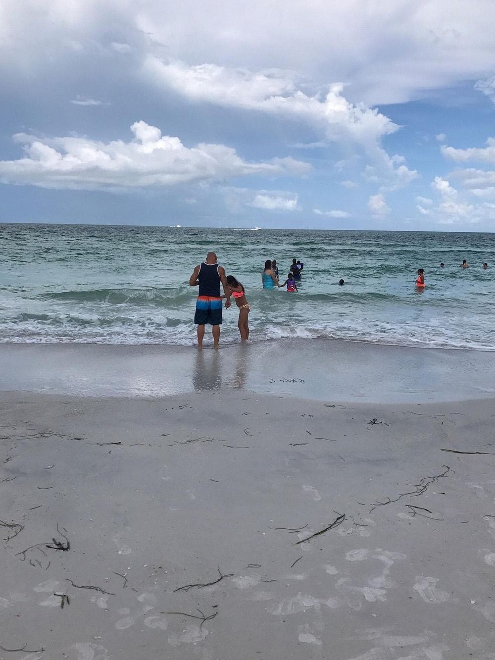 Beach with people swimming and playing in the ocean, family enjoying seaside vacation under cloudy sky.