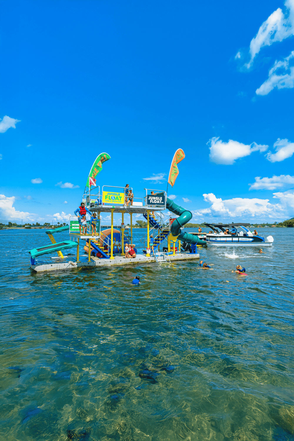 Floating water park with slides and people enjoying water activities on a bright, sunny day.