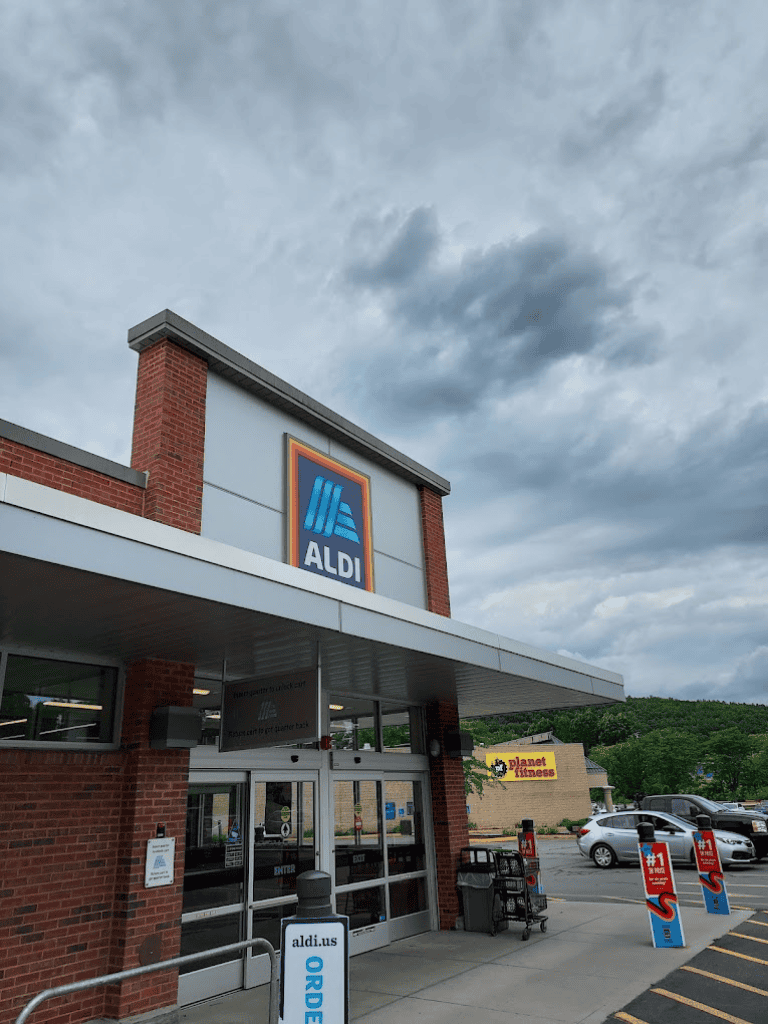 Aldi grocery store entrance with shopping carts and parking lot under cloudy sky.