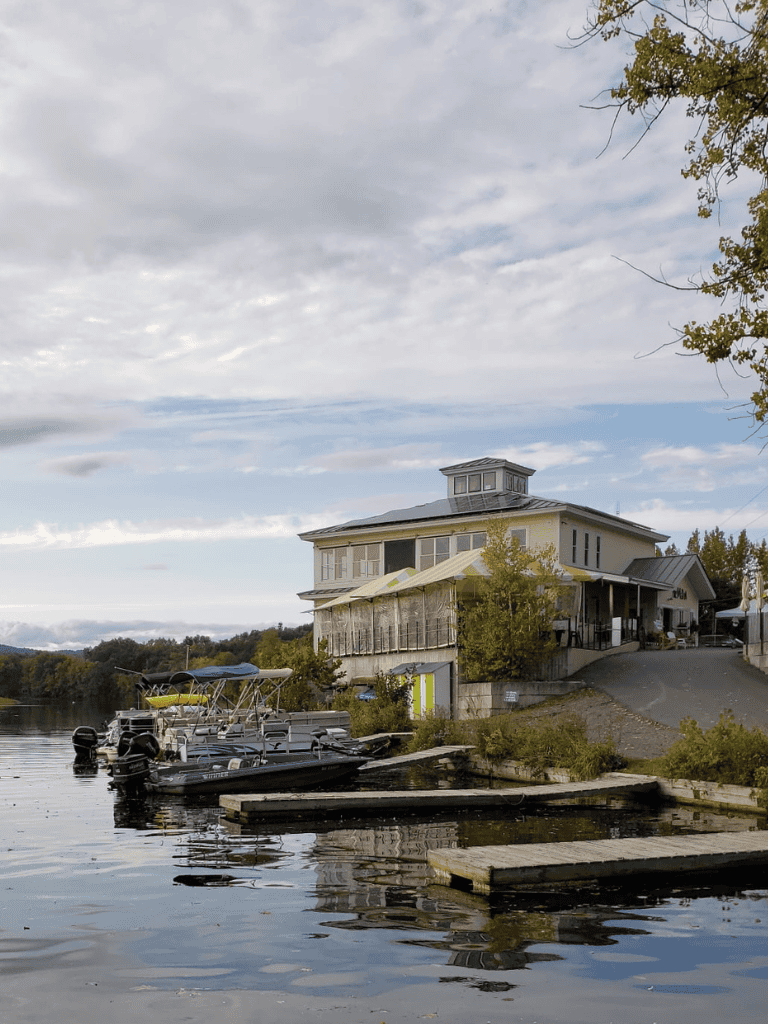 Boathouse on waterfront with boats docked, scenic outdoor scene, and cloudy sky in the background.