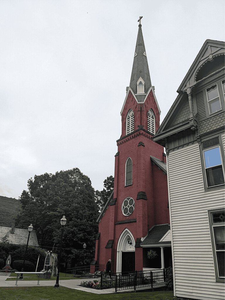Vivid red church with tall steeple, historic architecture, surrounded by greenery and decorative street lamps.