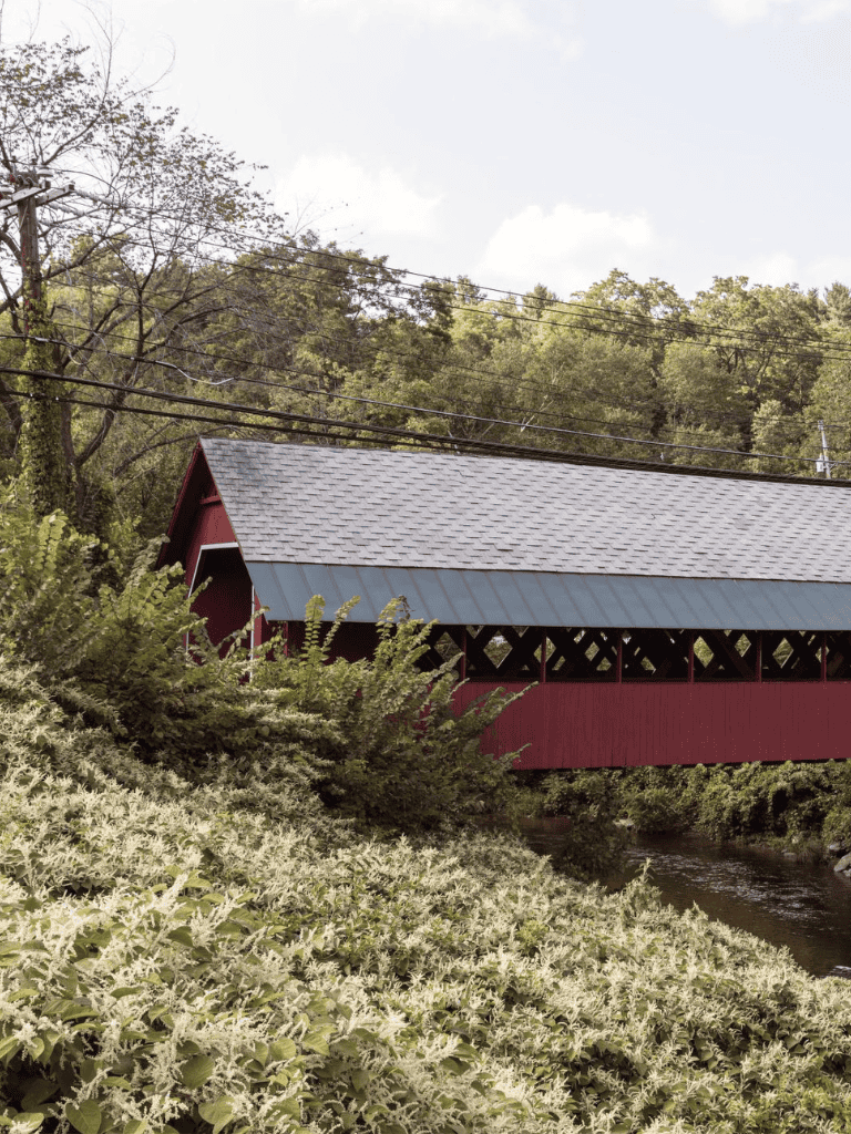 Covered bridge in a lush, green countryside setting with stream, under a clear sky.