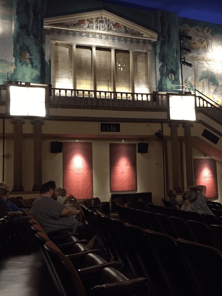 Ancient Greek-themed theater interior with audience, murals, and decorative columns for cultural events and performances.