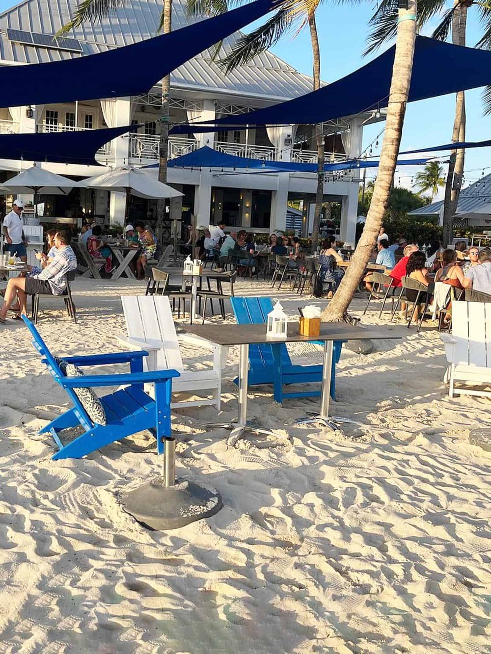 Beachside dining at Quest For Directions, with shaded seating and a lively crowd enjoying the seaside atmosphere.
