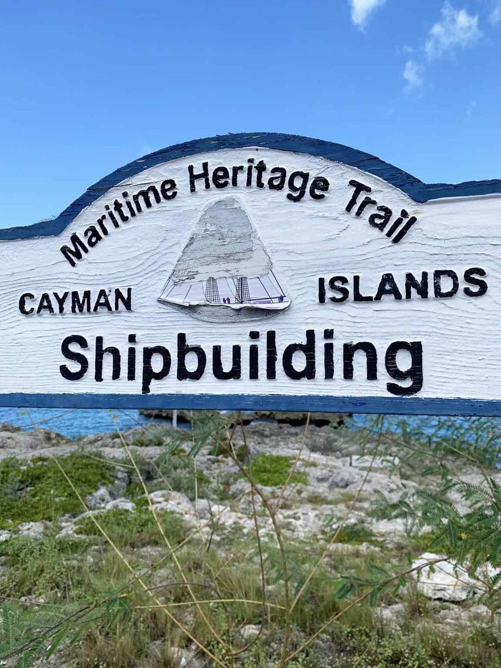 Maritime Heritage Trail Cayman Islands shipbuilding sign, coastal outdoor scene, clear blue sky, and nature backdrop.