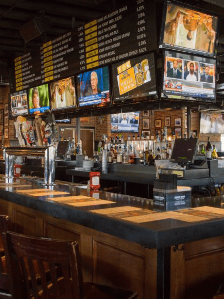 A cozy bar with multiple TV screens displaying news and sports, set in a warm brick interior for sports fans and social gatherings.