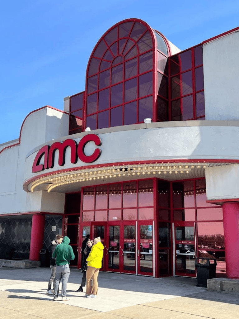 AMC theater entrance with red architecture and people standing outside.