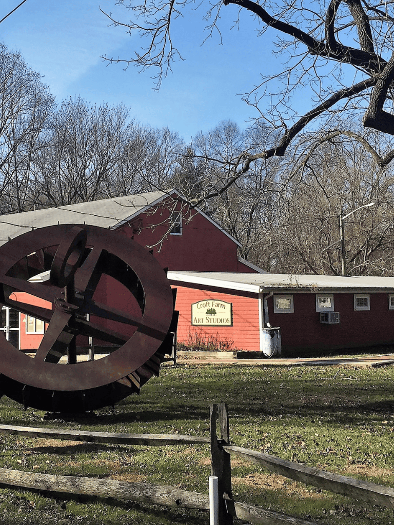 Rustic farm art studio with metal sculpture and red barn, scenic outdoor rural setting.