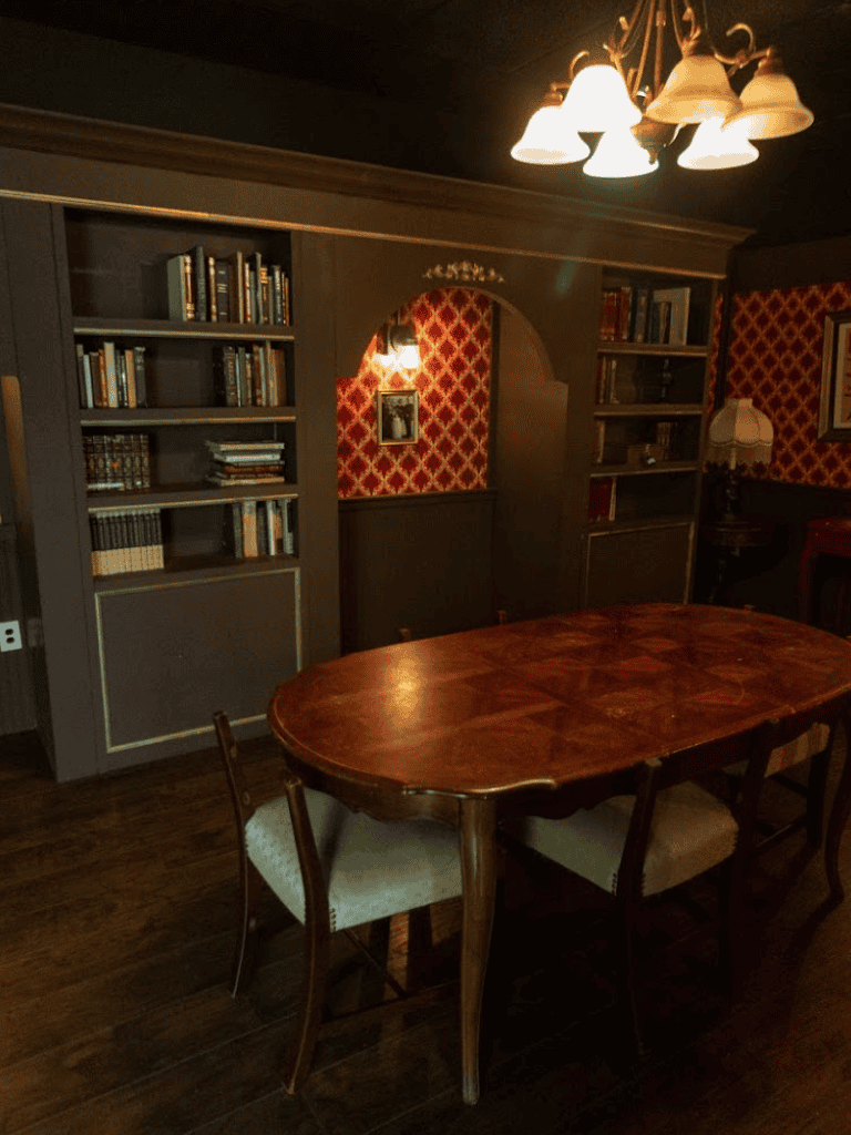 Vintage dining room with dark wood furniture and bookshelves, cozy lighting, and elegant wallpaper accents.